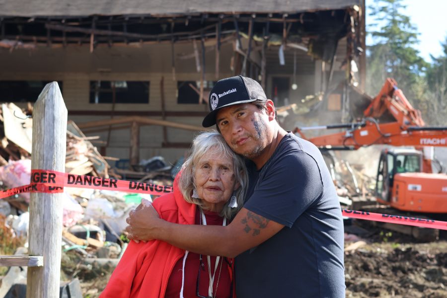 <who> Photo Credit: Nora O’Malley Local Journalism Initiative Reporter </who> Janet Webster, 83, stands with her son Hudson in front of a demolished Old Christie. Webster went to the residential school for nine years.